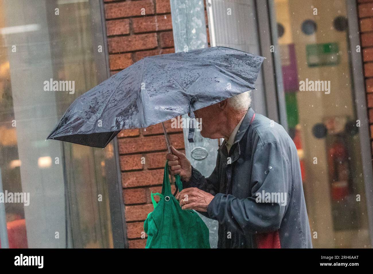 Älterer Mann mit beschädigtem Schirm in Southport, Merseyside. Wetter in Großbritannien. August 2023; Wetter in Großbritannien. Warmer Regen um 19 °C, während die Käufer in Southport durchnässt werden. Ausbrüche von Regenregen in Nordengland und Wales heute Nachmittag, stark und donnernd. Wechselnde Wolken, sonnige Wellen und verstreute Schauern im Nordwesten. Stockfoto