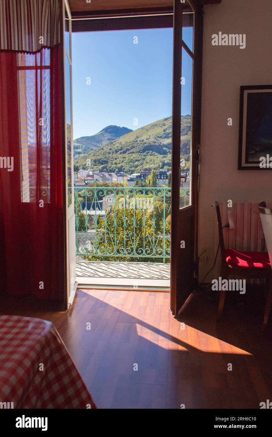 Offene Tür zum Balkon mit Blick auf die Berge, Lourdes, Frankreich. Gemütliches Apartment-Interieur. Wohnzimmer mit stilvoller Einrichtung. Sonniger Tag in Frankreich. Stockfoto