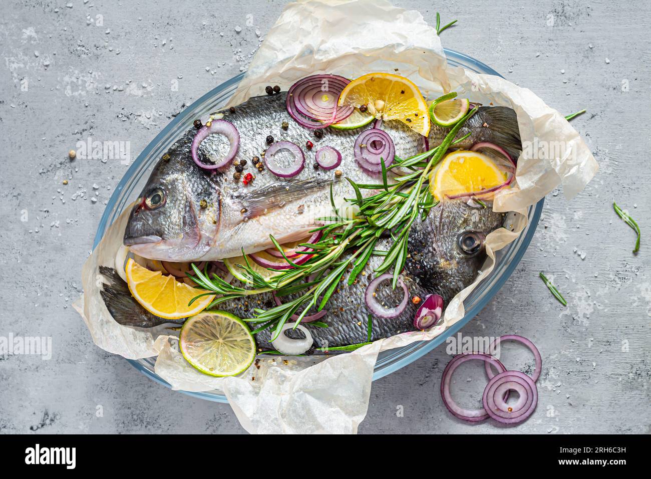 Frischer Fisch, dorado. Roher dorado mit Kräutern, Gewürzen und Zitronen- und Limettenscheiben, die auf grauem Hintergrund zubereitet werden können. Draufsicht. Frischer Fisch in einem Glasgebäck Stockfoto