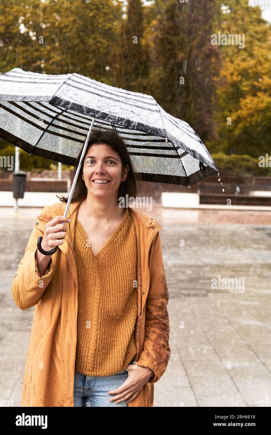 Mid Woman mit Regenschirm, die an einem Regentag in die Kamera schaut Stockfoto