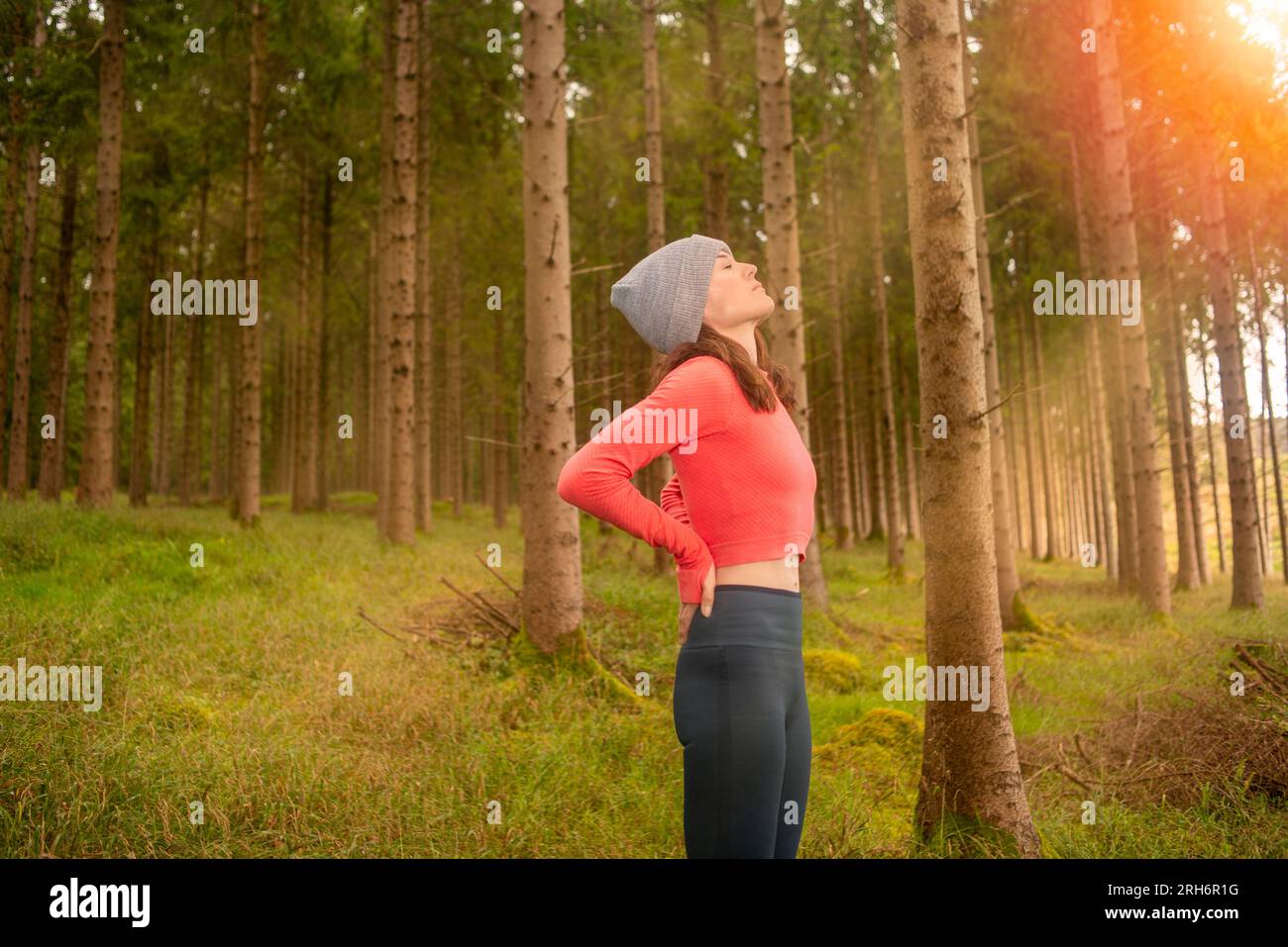 Sportliche Frau, die sich nach sportlichen Übungen im Wald den Rücken vor Schmerzen bewahrt. Stockfoto