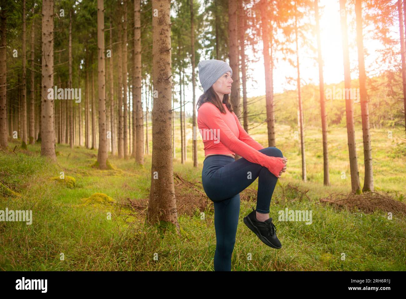 Sportliche Frau, die Beindehnungsübungen macht, draußen im Wald. Outdoor-Trainingskonzept. Stockfoto