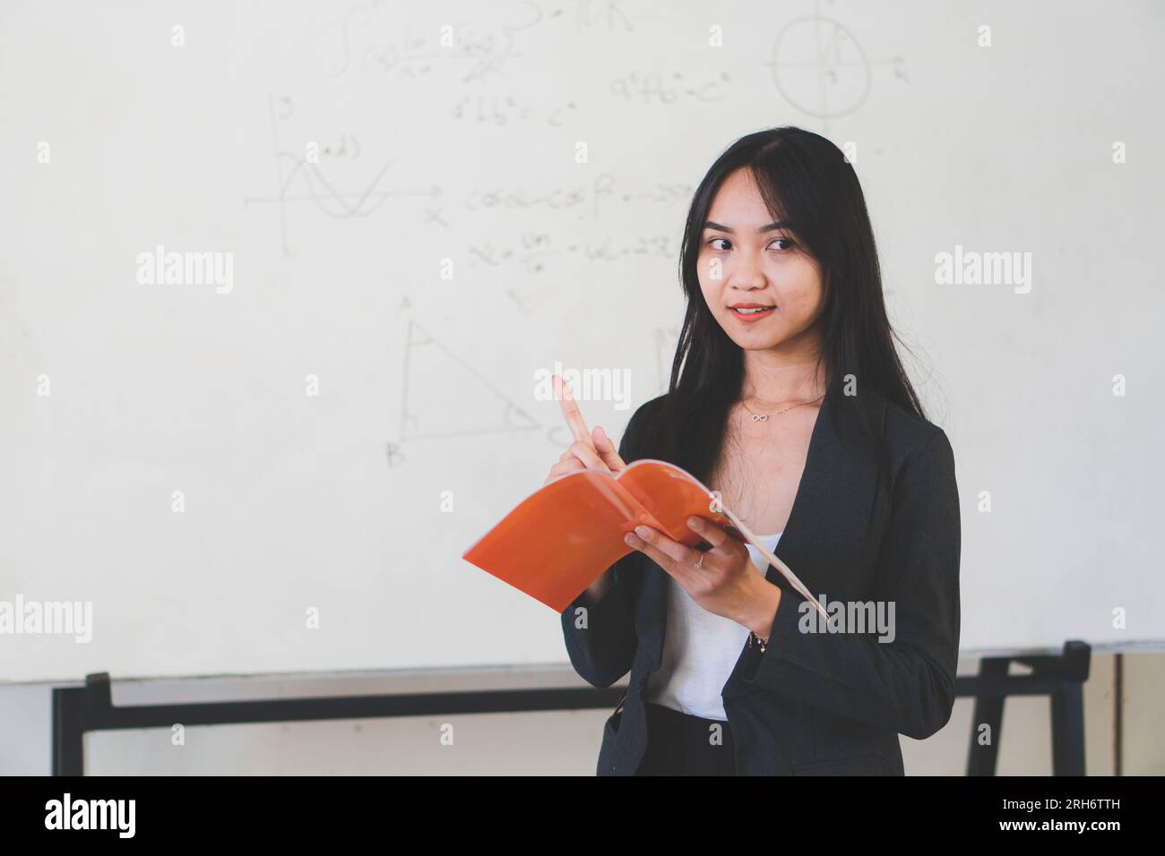 asiatischer Lehrer mit Buch auf Whiteboard-Hintergrund Stockfoto