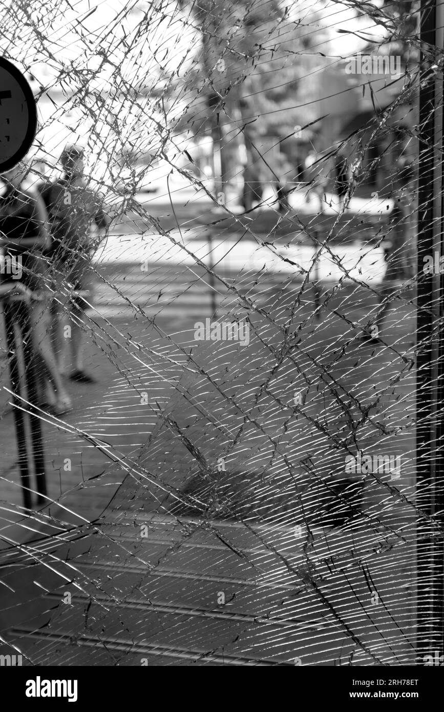 Zerbrochenes Glas an der Eingangstür des Supermarkts. Moderne, modische gepanzerte Glastür in einem Netz aus Rissen nach einem Akt des Vandalismus während des Krieges. Stockfoto