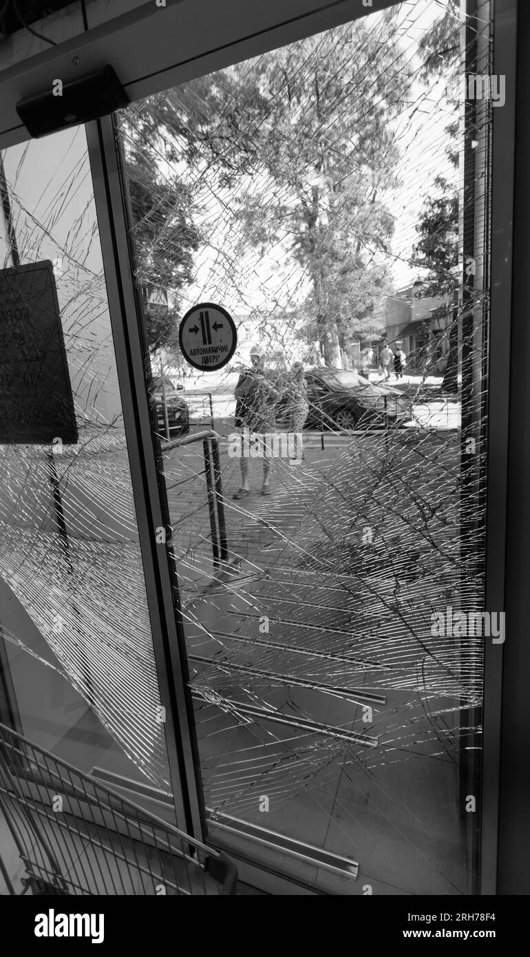 Zerbrochenes Glas an der Eingangstür des Supermarkts. Moderne, modische gepanzerte Glastür in einem Netz aus Rissen nach einem Akt des Vandalismus während des Krieges. Stockfoto