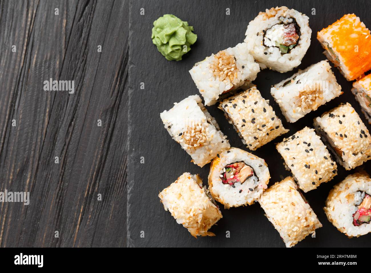 Sushi-Brötchen mit Lachs, Thunfisch, Kaviar, Sesamsamen auf einer schwarzen Steinplatte, Nahaufnahme. Stockfoto