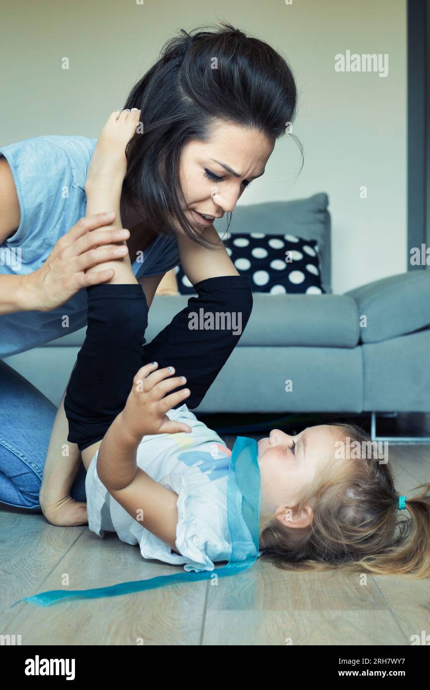 Das körperliche Spiel von Mutter und Tochter im Wohnzimmer: Klettern, fliegen, freudig lernen, voller Liebe und Herausforderungen Stockfoto