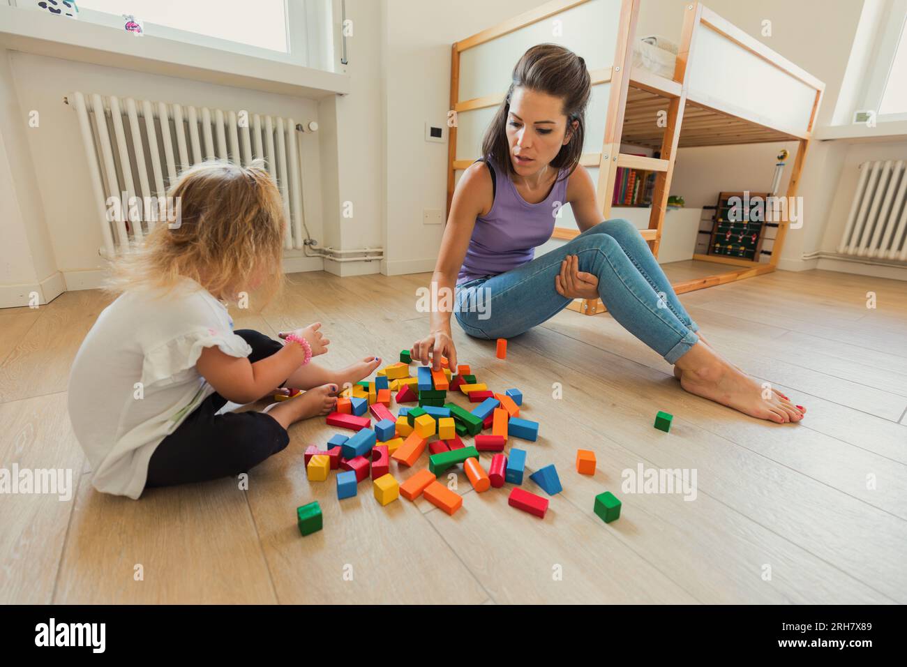 Im Spielzimmer erkunden eine Mutter und ihr blondes Kind Holzspielzeug, lernen und lachen, fördern die Kreativität und fördern die Bindung Stockfoto