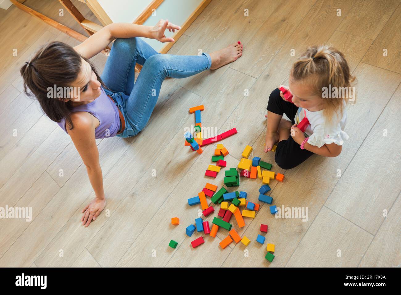 Junge Frau und blondes Kind spielen im Schlafzimmer mit bunten Holzspielzeugen, knüpfen sich an, lernen, Spaß haben durch praktische Erfahrungen Stockfoto