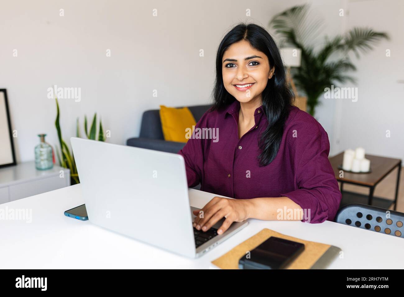 Porträt einer fröhlichen indischen Geschäftsfrau, die zu Hause mit einem Laptop in die Kamera lächelt Stockfoto