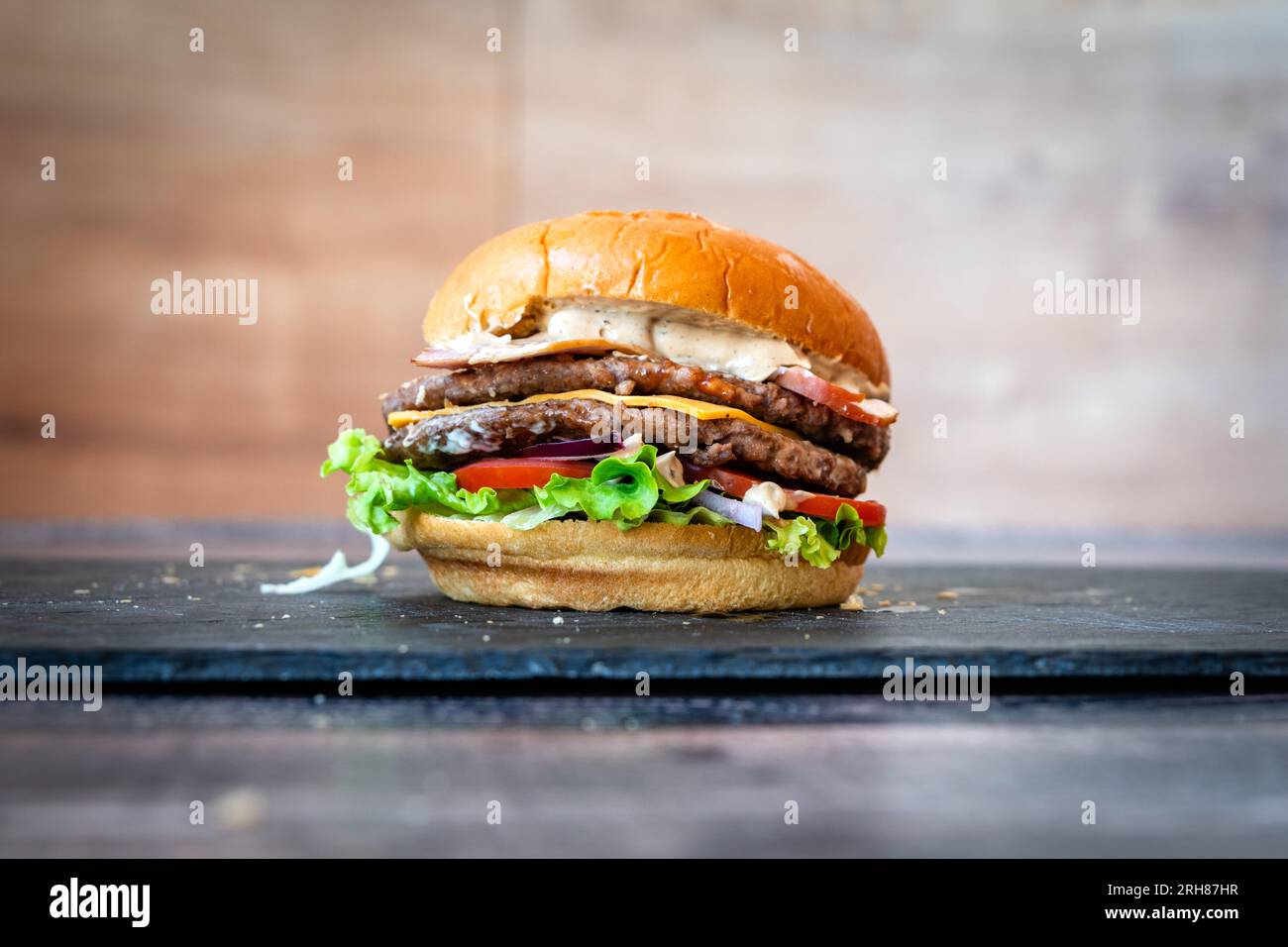 Rinderburger mit Sesamsalat, Brötchen, Tomaten, Cheddar auf schwarzem Hintergrund Stockfoto