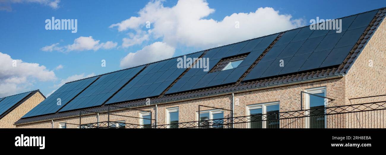 Neubauten mit Sonnenkollektoren auf dem Dach vor einem sonnigen Himmel , Nahaufnahme eines neuen Gebäudes mit schwarzen Sonnenkollektoren in den Niederlanden Stockfoto