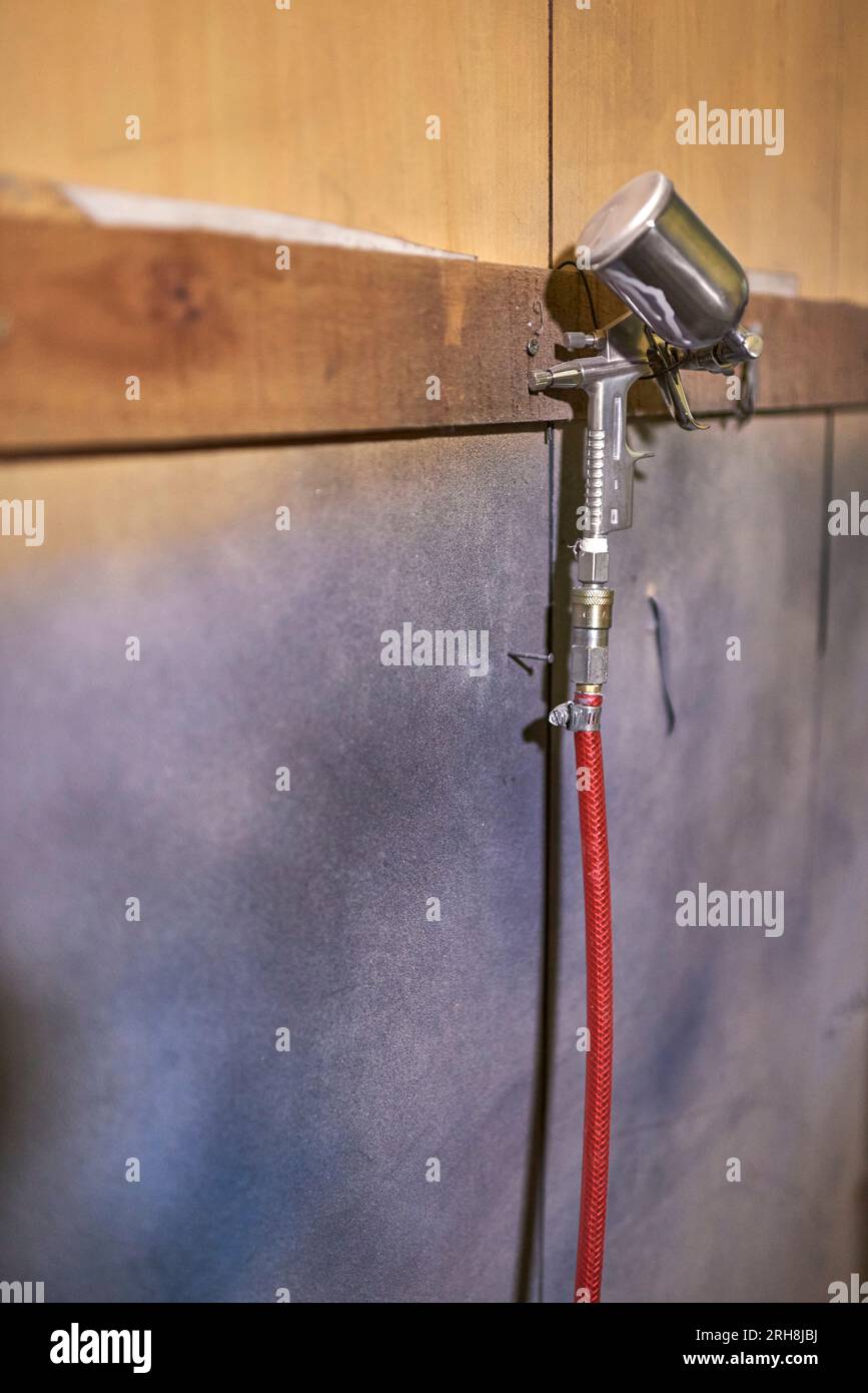 Spritzpistole hängt an einer Werkstattwand. Detail eines echten Arbeitsbereichs, Komposition mit Kopierbereich. Stockfoto