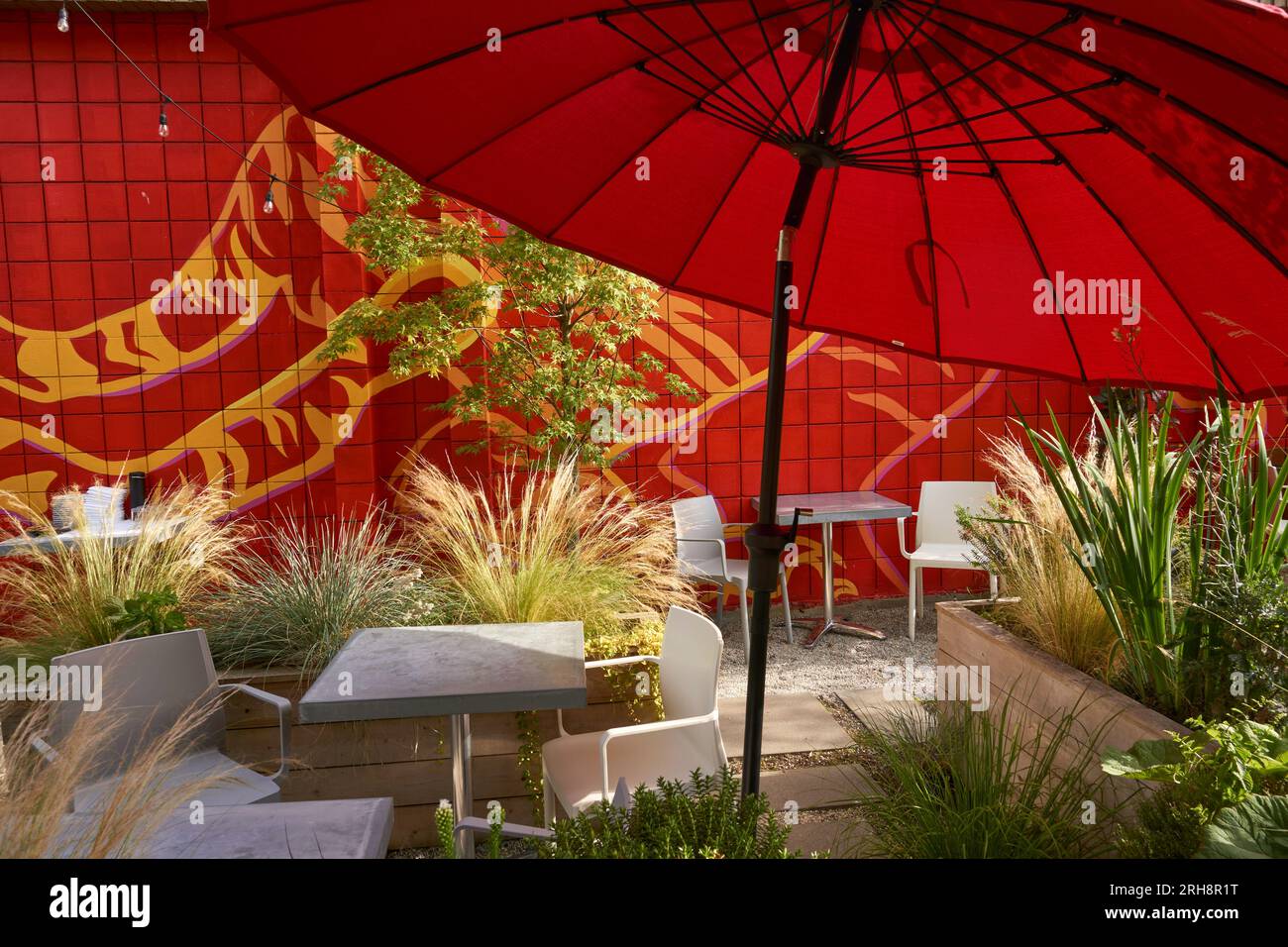 Gemütlicher Sitzbereich im Restaurant im Freien mit rotem Sonnenschirm und Pflanzen Stockfoto