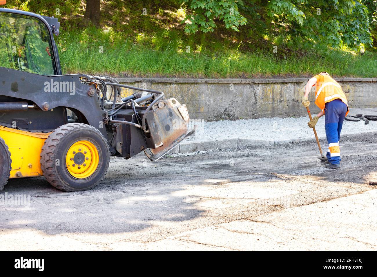 Ein Straßenarbeiter räumt während der Reparatur einen Teil einer alten Straße mit einem Fräser und einer Schaufel. Stockfoto