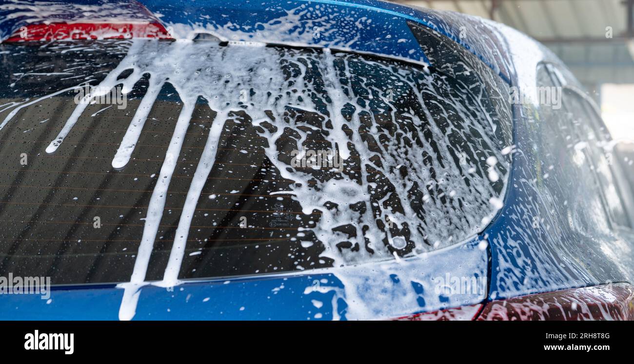 Blaue Autowaschanlage mit weißem Seifenschaum und professioneller Autowartung. PKW-Reinigungsservice-Konzept. Fahrzeugreinigung. Schaumstoff-Waschwagen-Details Stockfoto