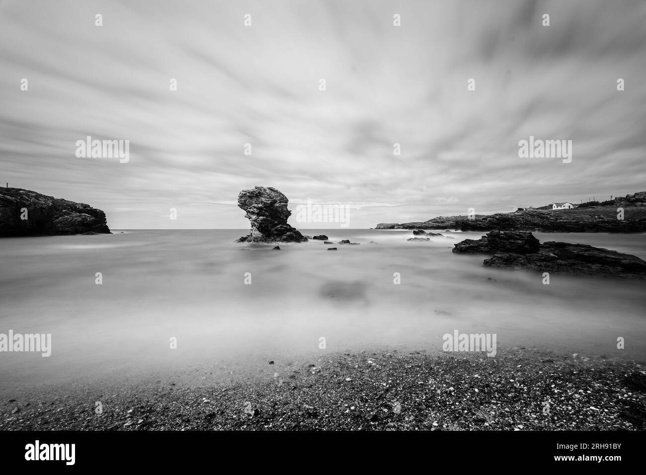 Kleiner Felsblock direkt an einem Kieselstrand in Wales. Eine lange Exposition verleiht dem Meer ein geschmeidiges seidiges Aussehen. Stockfoto