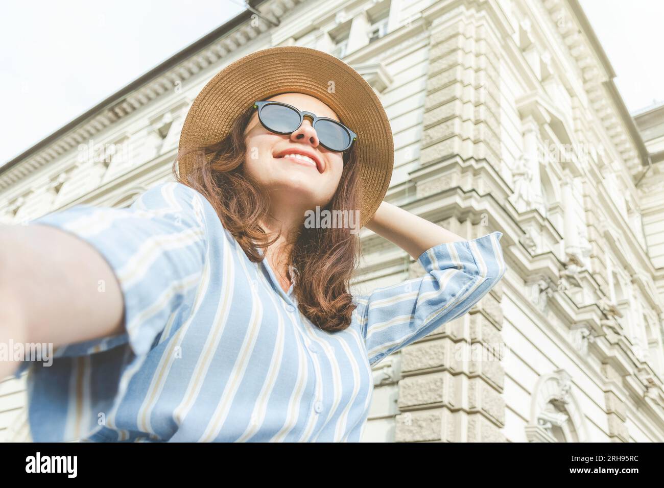 Modische Frau mit Sonnenbrille und Sonnenhut, die bei einem Spaziergang durch die Stadt ein Selfie macht. Stockfoto