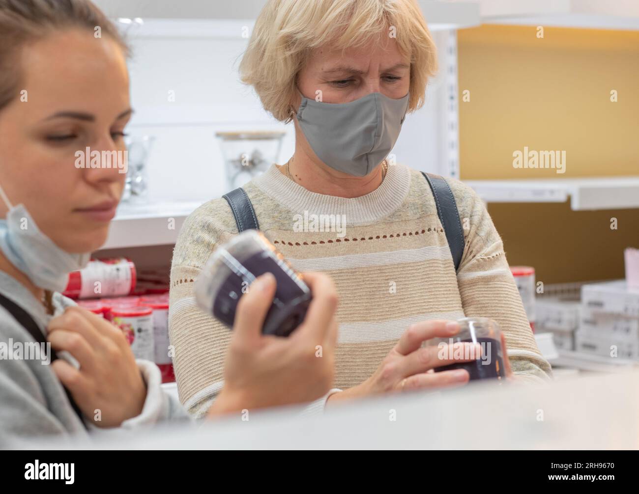 Zwei Frauen mit Schutzmaske kaufen im Einzelhandel ein. Die Menschen pflegen sich auch nach der Coronavirus-Pandemie weiter selbst. Echte Menschen. Stockfoto