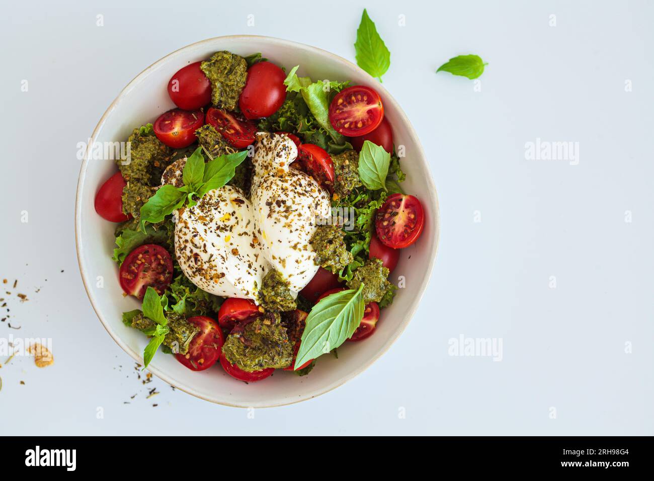 Burrata-Salat mit Kirschtomaten, Pesto und Gewürzen in einer Schüssel auf weißem Hintergrund, Draufsicht. Stockfoto