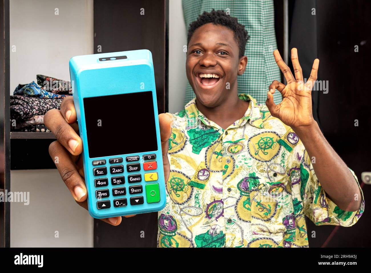 Bild eines schwarzen afrikaners, der aufgeregt steht, während er eine POS-Maschine, ein POS-Terminal, ein technisches Gerät hält Stockfoto
