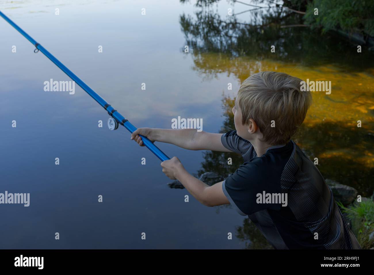 Ein Teenager auf einem Fluss wirft eine Angelrute, um Fische zu fangen. Sportfischen auf dem Fluss im Sommer. Stockfoto