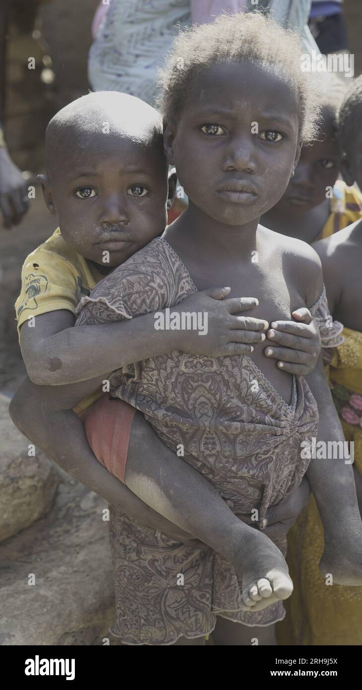 Wunderschönes Bild einer afrikanischen Schwester, die ihren jüngeren Bruder auf dem Rücken hält. Ähnelt dem tief verwurzelten Gefühl der Fürsorge in unserer menschlichen Natur. Armut. Stockfoto