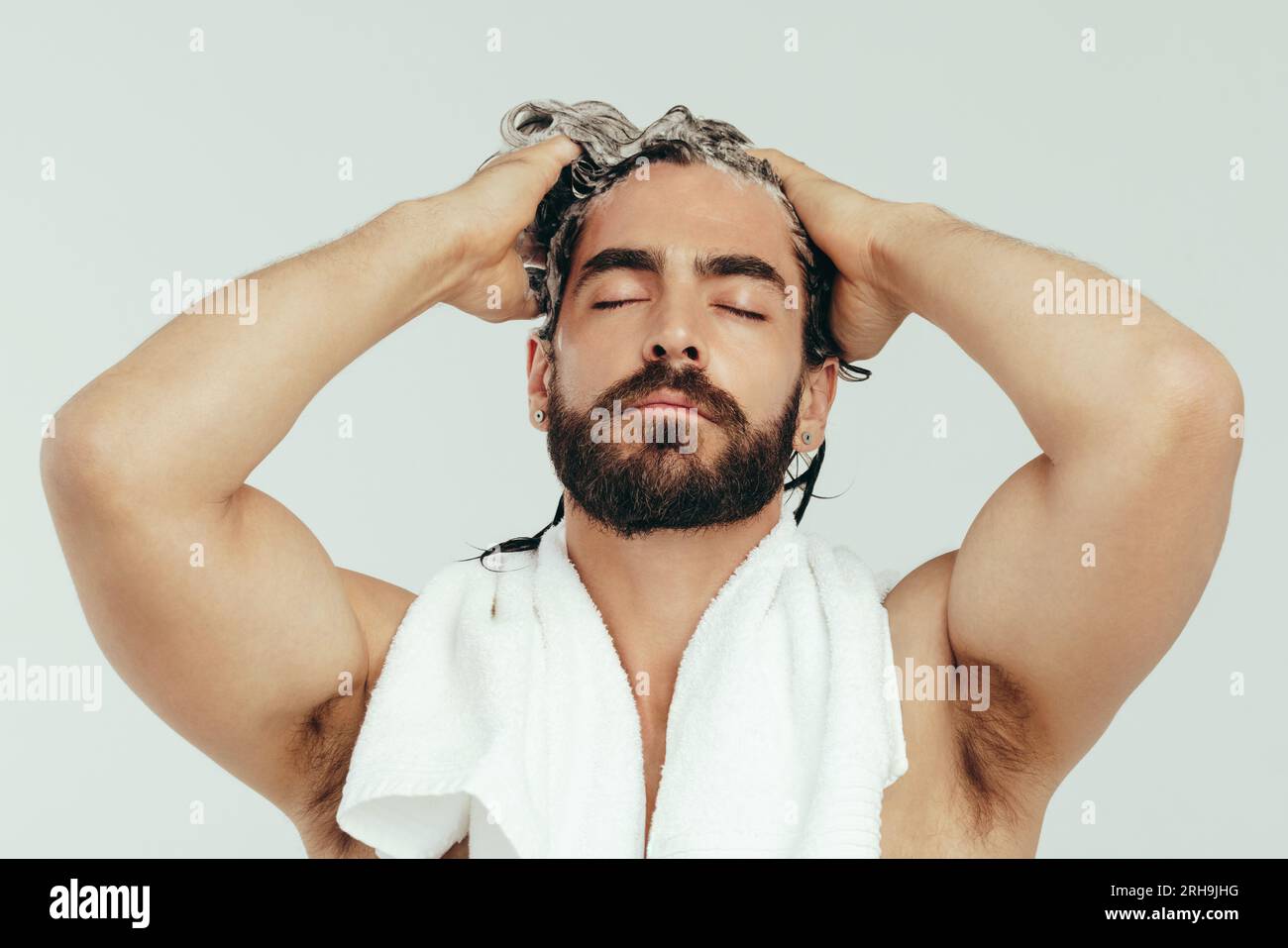 Mit geschlossenen Augen trägt ein Mann Shampoo auf sein Haar auf und massiert es vorsichtig in seine Kopfhaut. Ein junger Mann, der sich mit einem Glibber in seine Körperpflege einmischt Stockfoto