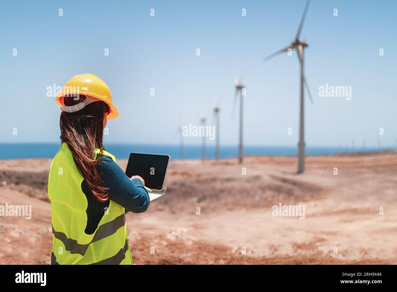 Ingenieurin, die mit einem Computer-Tablet auf dem Betriebsgelände eines alternativen Windenergieerzeugers arbeitet - Industrie- und Technologiekonzept Stockfoto