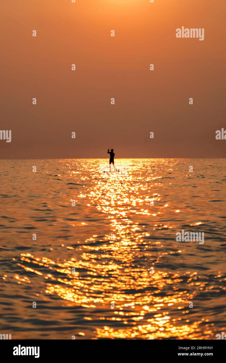 Farbenfroher Himmel bei Sonnenuntergang mit der Silhouette eines Mannes, der auf dem Paddleboard auf dem Meer surft. Stockfoto