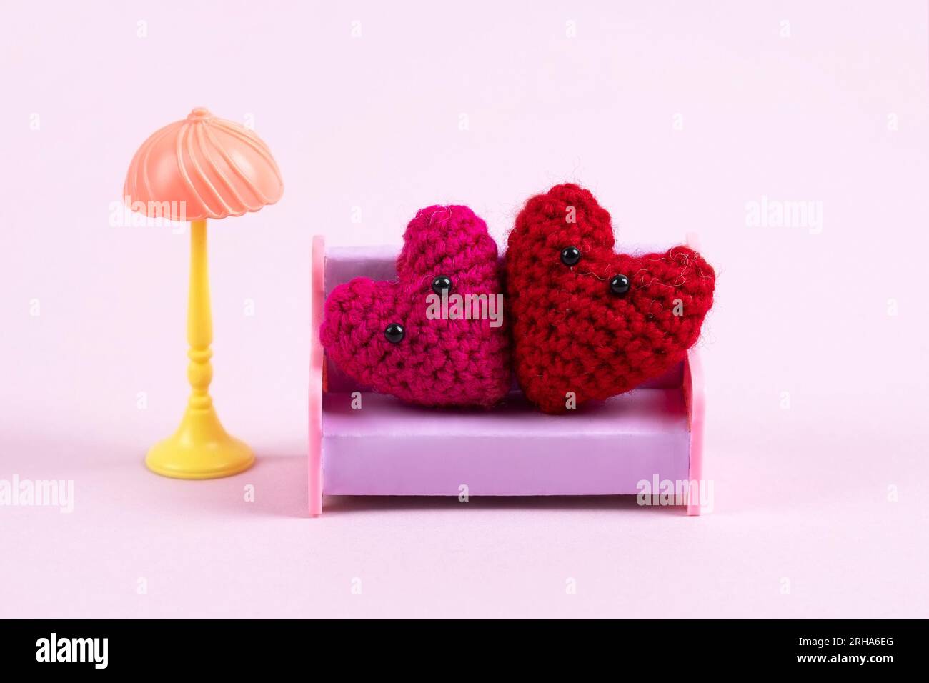 Komposition aus einer Familie gestrickter roter Herzen, die auf einem Spielzeugsofa auf einem lilafarbenen Hintergrund sitzen. Symbol der Liebe. Kinderspielzeug, Hobbys und Zugang stricken Stockfoto