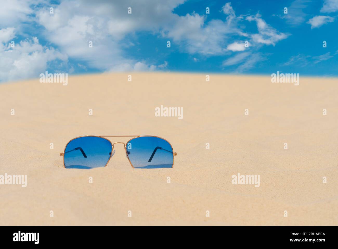 Blaue Sonnenbrillen liegen auf dem Sand vor dem blauen Himmel. Sommerurlaub, Reise- und Tourismuskonzept. Sommerruhe. Weihnachtszeit Stockfoto