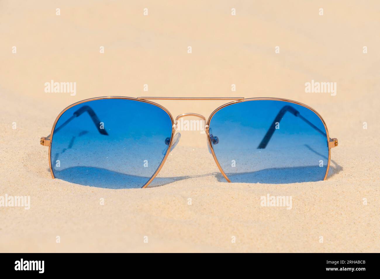 Blaue Sonnenbrillen liegen auf dem Sand vor dem blauen Himmel. Sommerurlaub, Reise- und Tourismuskonzept. Sommerruhe. Weihnachtszeit Stockfoto