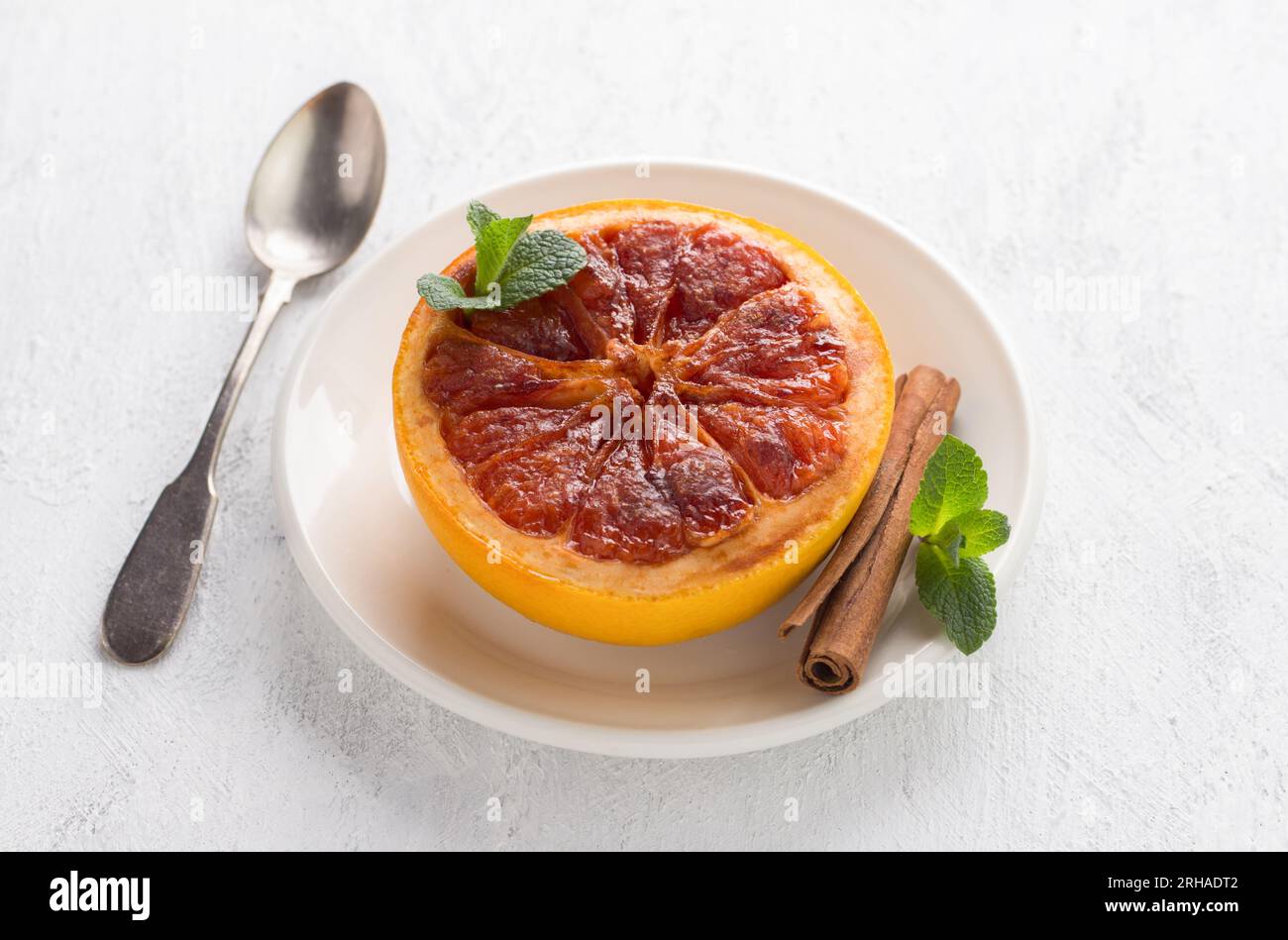 Gebackene Grapefruit mit braunem Zucker und Zimt garniert mit Minze auf hellgrauem Hintergrund. Köstliches, gesundes Dessert oder Frühstück. Stockfoto