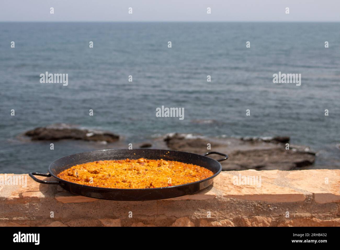 Serviert eine Paella am Meer mit der Palette und den Händen Stockfoto