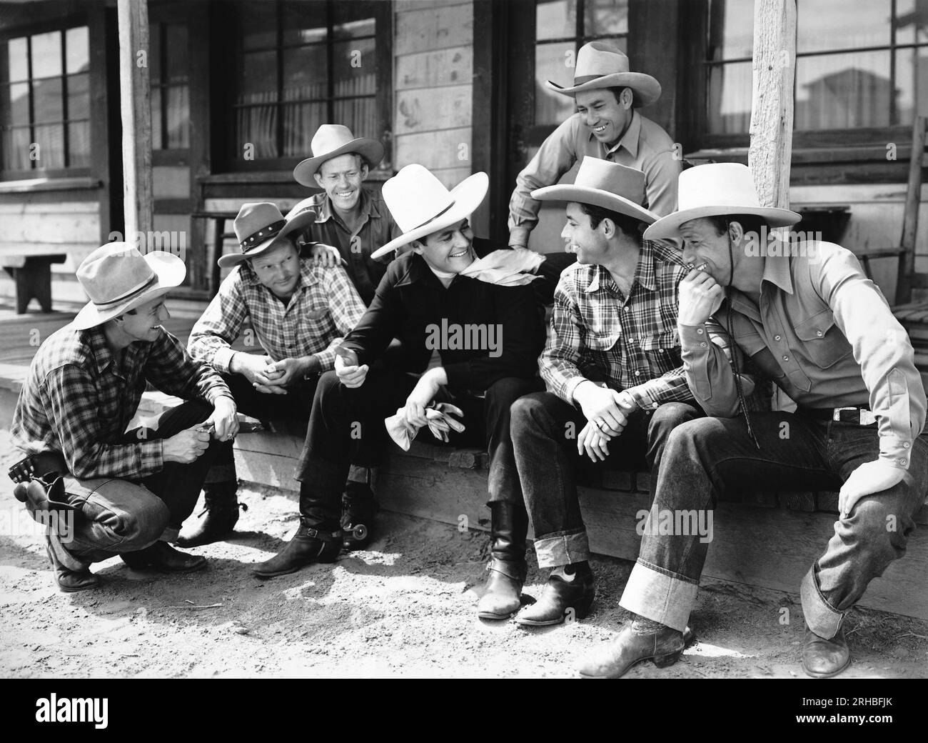Hollywood, Kalifornien: ca. 1925 Cowboy-Schauspieler Tom Mix, der auf einer Veranda mit einer Gruppe Cowboys gesessen und sich unterhalten hat. Stockfoto