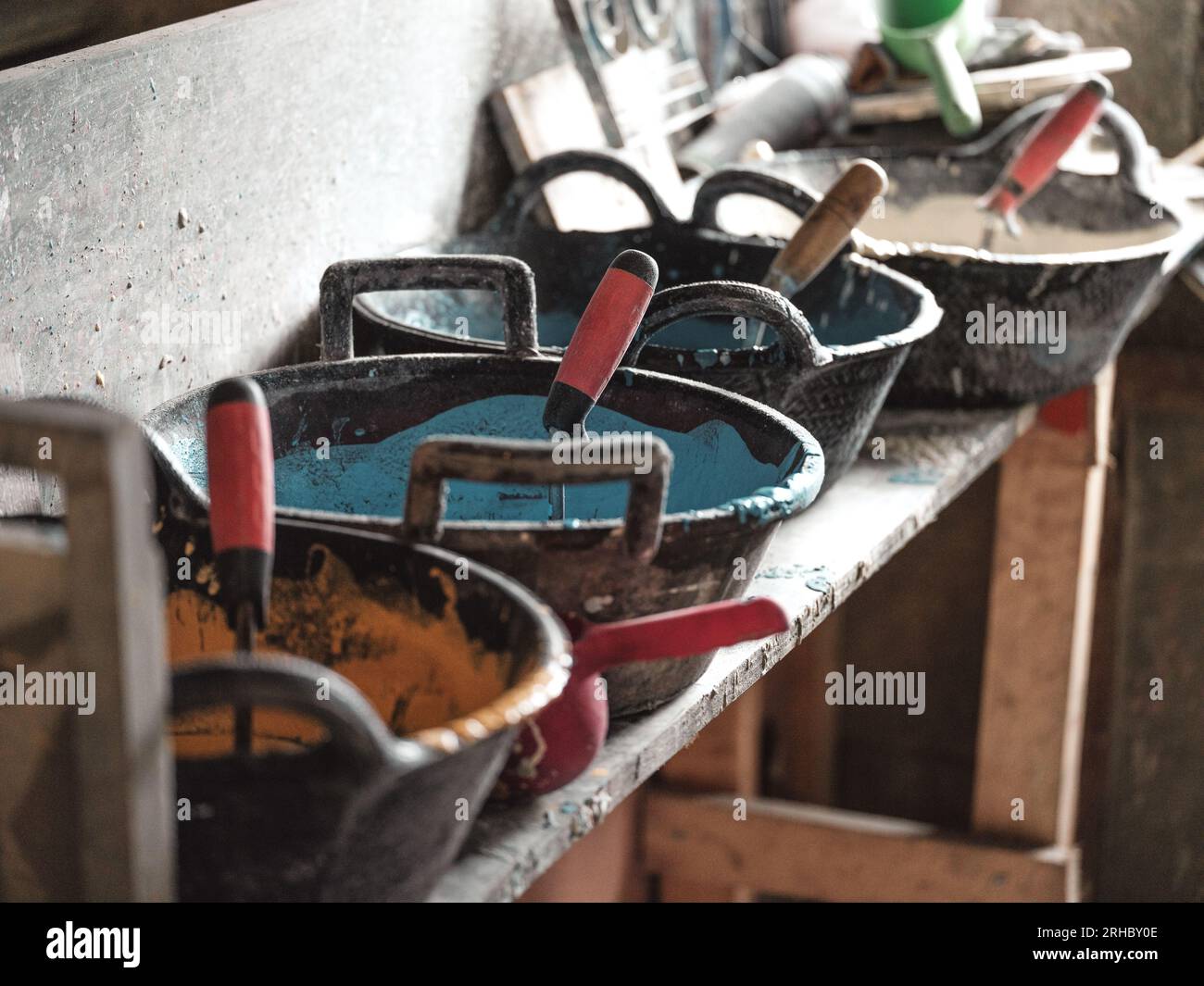 Großer Schüssel mit mehrfarbiger Keramikglasur und Rollen auf schäbigem Holzregal in der Werkstatt mit selektivem Fokus aus hohem Winkel Stockfoto