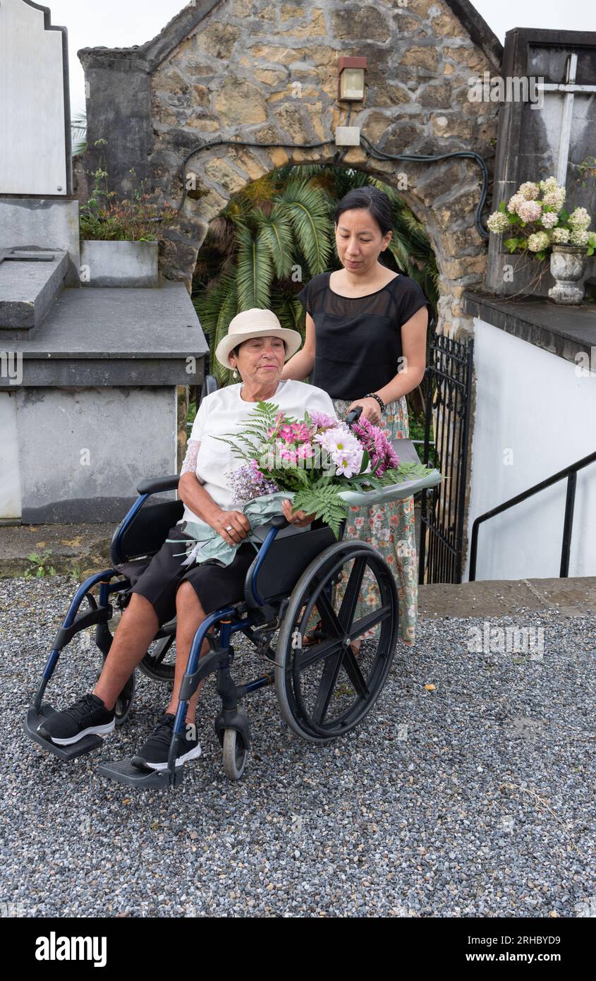 Mädchen mit behinderter Frau, die Blumen auf den Friedhof trägt Stockfoto