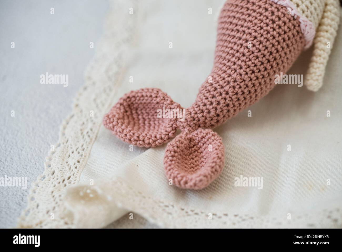 Nahaufnahme eines gehäkelten Amigurumi-Meerjungfrauenschwanzes auf einer Tischdecke aus Spitze Stockfoto