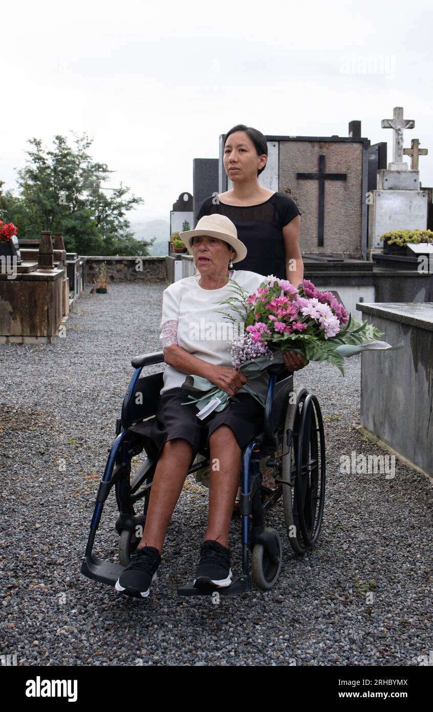 Mädchen mit behinderter Frau, die Blumen auf den Friedhof trägt Stockfoto