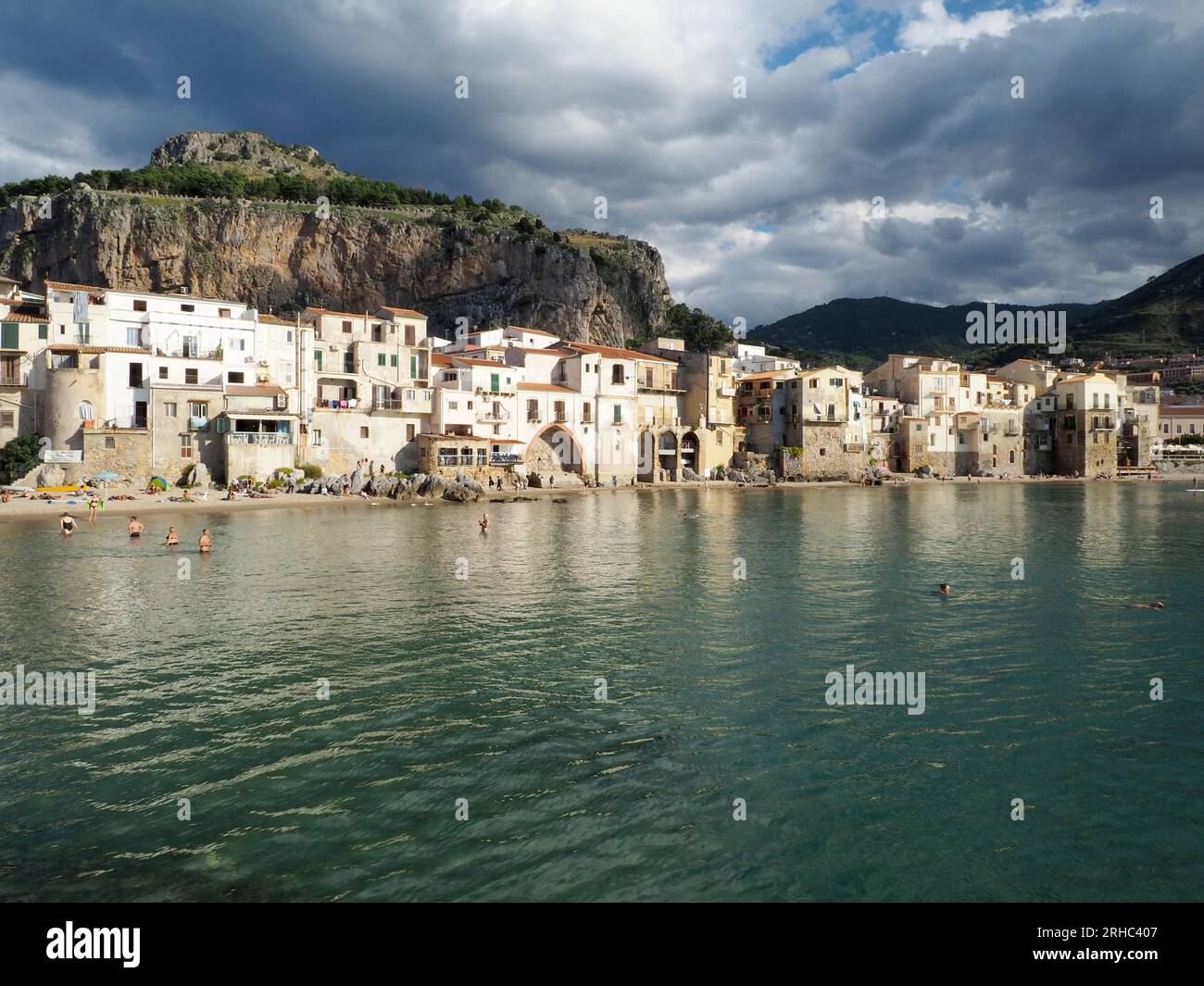 Der Strand und die Küste von Cefalu mit Menschen, die im Meer schwimmen. Stockfoto