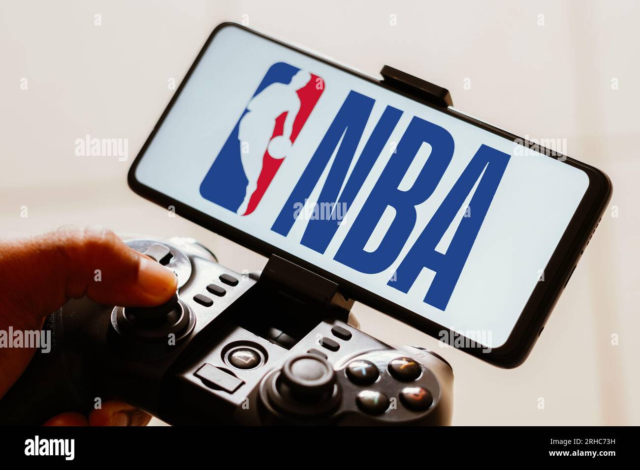 In dieser Fotoabbildung wird das Logo der National Basketball Association (NBA) auf dem Smartphone-Bildschirm angezeigt, während eine Person auf einem Joystick spielt. Stockfoto