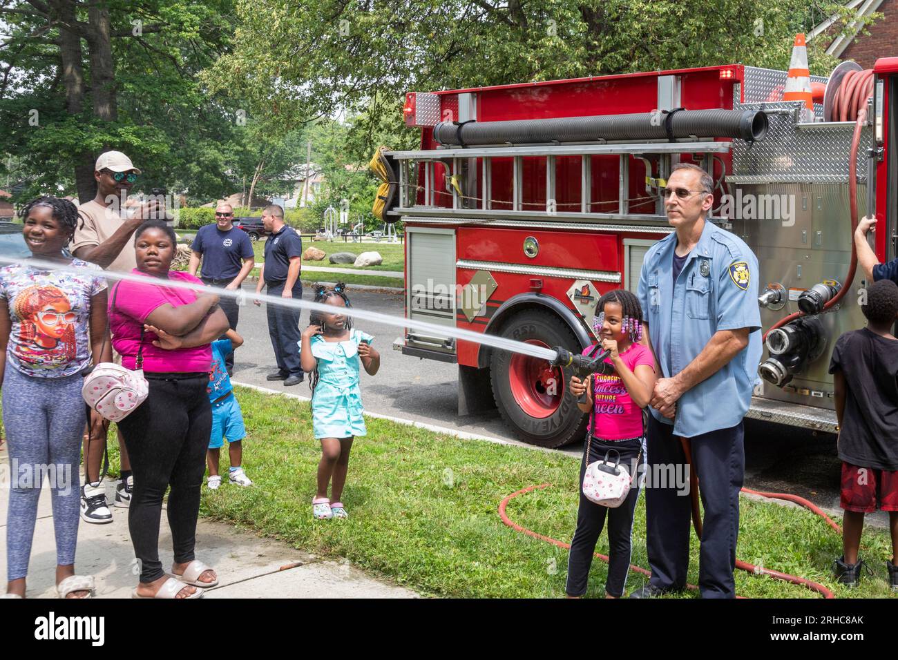 Detroit, Michigan - die Feuerwehr von Detroit erlaubt Kindern, einen Feuerwehrschlauch zu verwenden, während die Bewohner des Stadtviertels Morningside ein Picknick/eine Party veranstalten Stockfoto