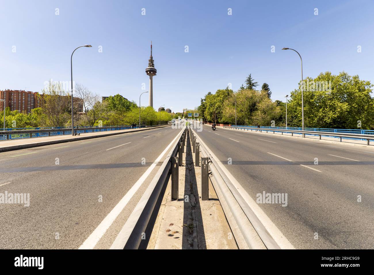Überqueren einer Brücke mit einem normalen Bürgersteig und einer Radspur auf einer Straße mit Fahrzeugverkehr und dem Telekommunikationsturm in Madrid Stockfoto