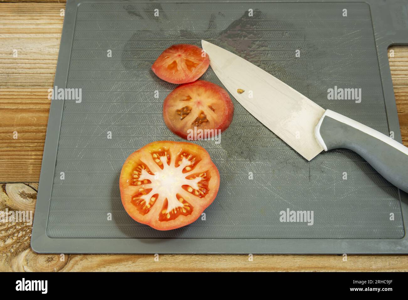 Ein paar reife Tomatenscheiben, die mit einem scharfen Messer auf einer grauen Kunststoffplatte geschnitten werden Stockfoto