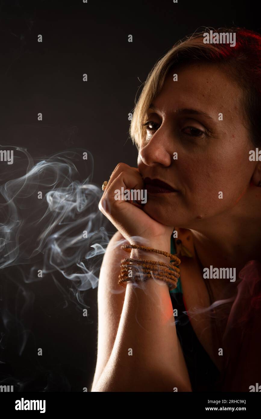Porträt einer attraktiven und schönen Frau mit der Hand am Kinn. Überall Räucherstäbchen. Isoliert auf schwarzem Hintergrund. Stockfoto