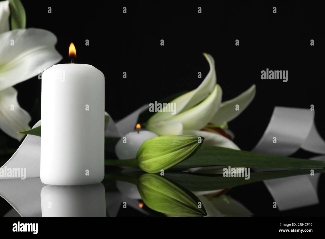 Weiße Lilien und brennende Kerzen auf schwarzer Spiegeloberfläche bei Dunkelheit, Nahaufnahme mit Platz für Text. Begräbnissymbole Stockfoto