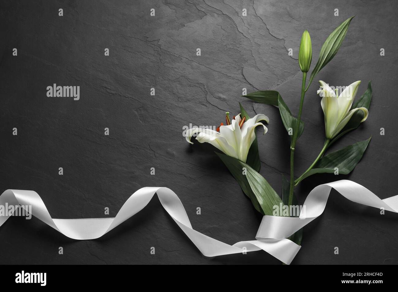 Weiße Lilien und Band auf schwarzem Tisch, flach liegend mit Platz für Text. Beerdigungssymbole Stockfoto