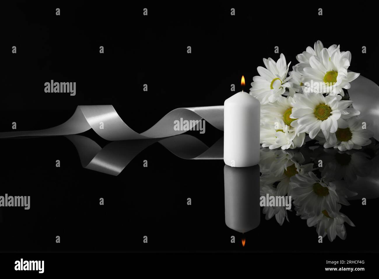 Brennende Kerze, weiße Chrysanthemen und Band auf schwarzer Spiegeloberfläche bei Dunkelheit, Platz für Text. Begräbnissymbole Stockfoto
