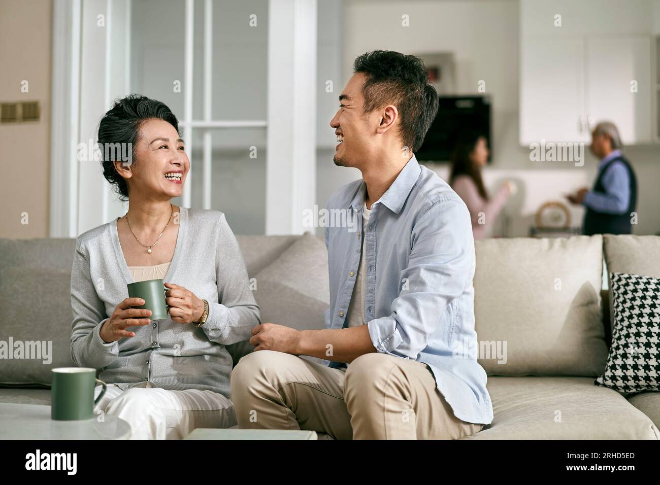 asiatischer erwachsener Sohn und ältere Mutter, die zu Hause auf der Couch im Wohnzimmer sitzen und ein angenehmes Gespräch führen Stockfoto